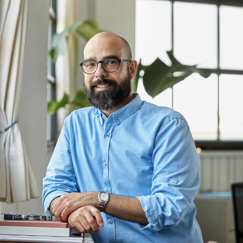 Homme en chemise bleue avec des lunettes appuyé sur une surface et souriant