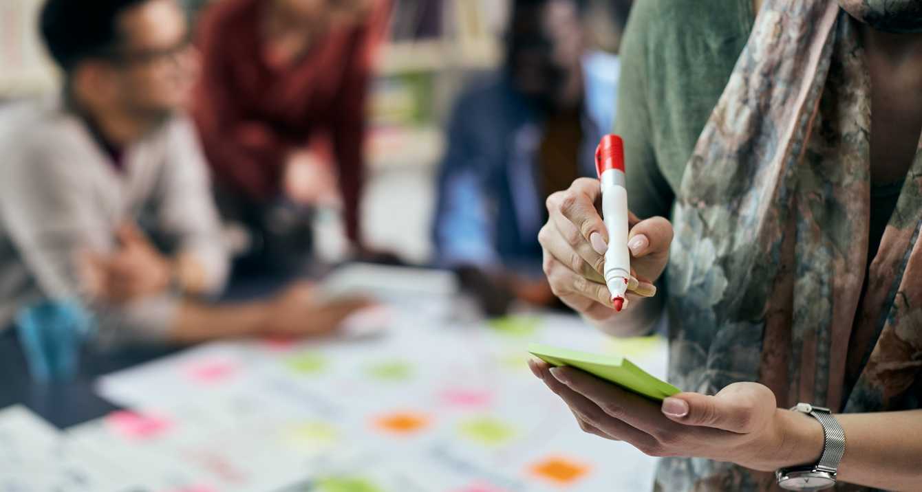 Primer plano de una persona creativa escribiendo en una nota adhesiva
durante una reunión de negocios