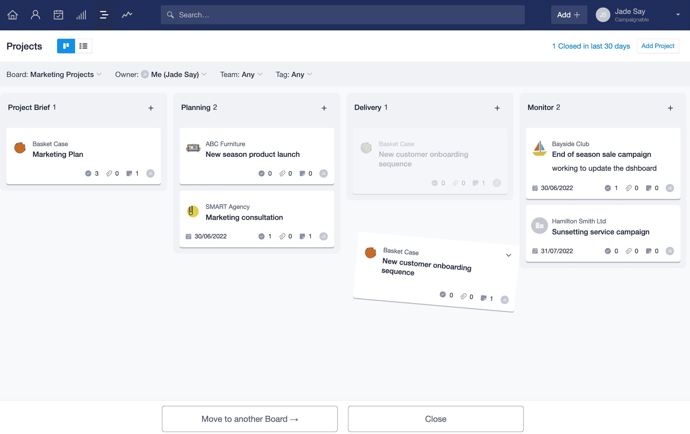 A visualização kanban do projeto é exibida com um cartão de projeto sendo arrastado para a parte inferior da página. Dois botões aparecem com a opção de fechar o projeto ou movê-lo para outro quadro