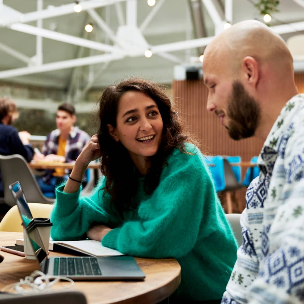 Dois colegas de trabalho conversam, sentados em frente a um laptop