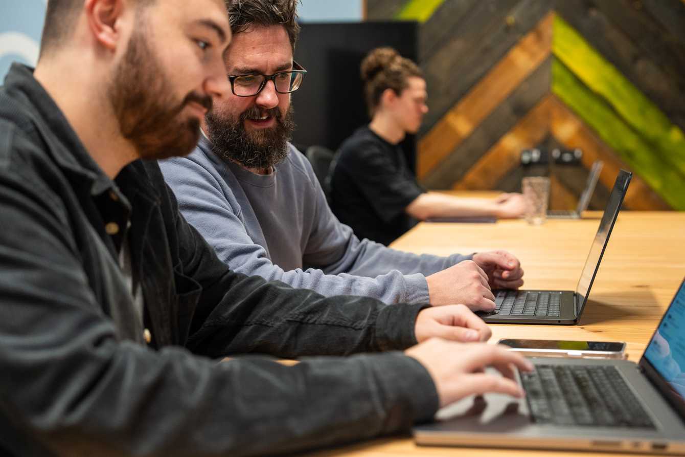 3 homens em uma mesa trabalhando em notebooks